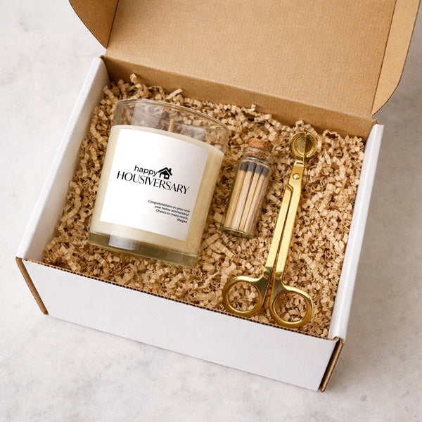 Home Anniversary Gift Happy Housiversary Candle Gift in a gift box with gold candle trimmer and jar of matches.